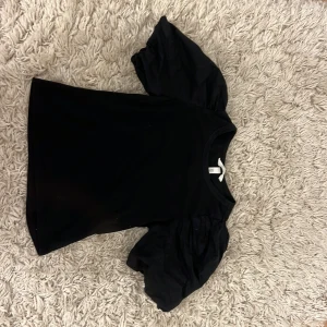 Svart topp med puffärmar från H&M - Svart topp från H&M i storlek XS med riktigt snygga puffärmar som ger en cool siluett. Toppen har rund halsringning och är gjord i mjuk bomull med ärmar i ett lite styvare tyg för extra volym. Perfekt för dig som vill sticka ut lite extra.
