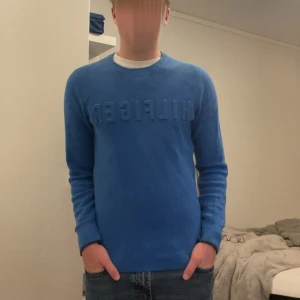 Blå stickad tröja Tommy Hilfiger XS - Snygg blå stickad tröja från Tommy Hilfiger i storlek XS. Tröjan har rund halsringning, långa ärmar och diskret Hilfiger-logga på bröstet samt vid ärmslutet. Perfekt för dig som gillar klassisk och stilren design.