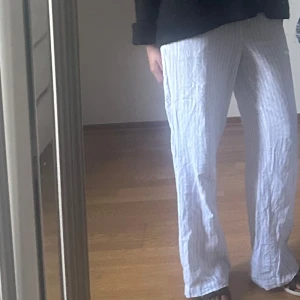 Randiga linnebyxor från BikBok - Luftiga linnebyxor från BikBok i vitt med tunna blå ränder. Byxorna har rak passform, elastisk midja och är perfekta för varma dagar. Sköna och stilrena med avslappnad vibe.
