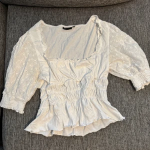 Vit blus med broderade ärmar från ASOS - Supersöt vit blus från ASOS DESIGN med broderade blommor på puffärmarna och smock vid ärmslut och midja.