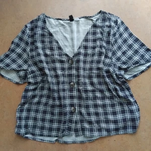 Rutig Blus  - Söt blus med knappar framtill i mörkblått/vitt. Kortärmad, v-ringad och något croppad i modellen, passar perfekt till högmidjade jeans. Från H&M Divided, storlek 40 men känns som 38 max. 100% viskos. Fint använt skick.