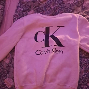 Vit Calvin Klein sweatshirt med logga - Vit sweatshirt från Calvin Klein med stor svart CK-logga och text på bröstet. Klassisk rund halsringning och långa ärmar. Mjuk och skön bomullsblandning, perfekt för en clean och stilren look.