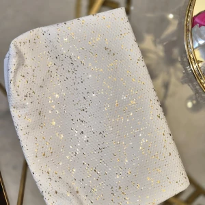 Vit kuvertväska med guldglitter - Snygg vit kuvertväska med glittriga guldprickar och struktur i materialet. Väskan har dragkedja och en stilren, modern look som sticker ut. Perfekt för dig som vill ha något extra till outfiten.