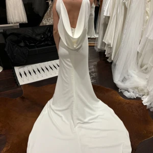 Bröllopsklänning, vit elegant med öppen rygg & superfint släp - Elegant vit bröllopsklänning med djup v-ringning fram och en snygg draperad öppen rygg baktill. Klänningen har figurnära passform och sitter som en smäck. Otroligt material som ej skrynklas. Använd 1 gång. Köpt på en brudklänningsbutik i Malmö. Pris går att diskutera. 