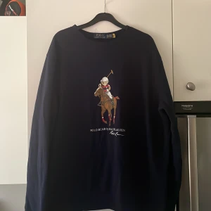 Mörkblå Polo Bear tröja Ralph Lauren  - Säljer en mörkblå långärmad tröja från Ralph Lauren i storlek XL fast passar både L och XL. Tröjan har bara blivit används ett fåtal gånger då den var lite stor för mig. Framsidan har ett stort tryck med den ikoniska Polo Bear. Tröjan har rund halsringning och är tillverkad i mjuk bomull, perfekt för en chill och stilren look. Nypris 1600kr mitt pris 900kr. 