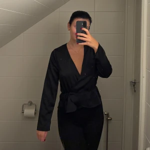 V-ringad omlottblus med knytning  - Säljer en fin svart blus med v-ringning och knytning i midjan från Bik Bok, (aldrig använd). 