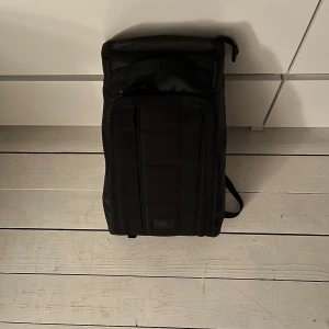 Svart ryggsäck med dragkedja - Säljer en stilren svart ryggsäck från DB med rejäla axelremmar och flera smarta fack. Väskan har en clean design, dragkedjor och är tillverkad i slitstark syntet. Perfekt för dig som vill ha en praktisk och snygg väska till vardagen eller resan.