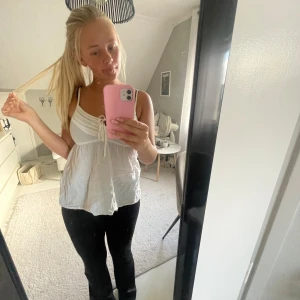 Vit linnetopp med knyt fram - Säljer en söt vit linnetopp med smala axelband och knytning framtill. Toppen har en lätt utsvängd passform och rynkade detaljer vid bysten som ger en romantisk vibe. Perfekt för varma dagar och enkel att styla med jeans eller kjol.