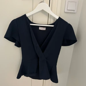 Svart omlottopp från Holly & White - Snygg svart omlottopp från Holly & White med korta puffärmar och v-ringning.