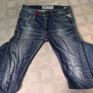 Replay Jondrill jeans blå, stl 31 - Säljer ett par Replay Jondrill jeans i klassisk blå tvätt med snygga slitningar och kontrastsömmar. Modellen har smal passform, fem fickor och coola detaljer som röd etikett och broderade bakfickor. Perfekta för dig som gillar en modern och stilren look.