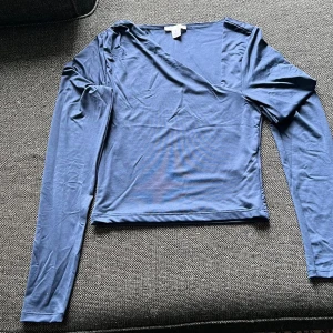 Blå omlottopp med lång ärm - Snygg blå omlottopp med lång ärm och v-ringning. Toppens material känns mjukt och stretchigt, perfekt för en chill och stilren look. Passar dig som gillar enkel men trendig stil.