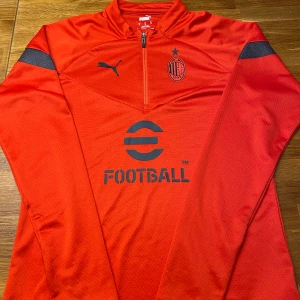AC Milan långärmad träningströja Puma M - Röd långärmad AC Milan träningströja från Puma med svart logga och klubbmärke på bröstet. Halv dragkedja framtill, svarta detaljer på ärmarna och tryckt 'eFootball' på magen. Tillverkad i lätt och ventilerande funktionsmaterial. Pris kan diskuteras via snabbaffär 