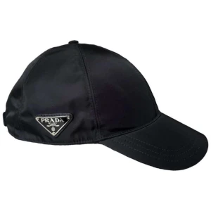 Svart keps från Prada i nylon - Snygg svart keps från Prada med klassisk böjd skärm och ikonisk metallogo på sidan. Tillverkad i glansig nylon som ger en modern och exklusiv känsla. Perfekt accessoar för att lyfta din streetstyle. Självklart äkta, kvitto och box finns. Tveka inte att skriva om ni har några frågor😃😃