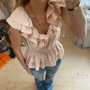 Ljusrosa volangtopp från H&M - Supersöt ljusrosa topp från H&M med volanger längs ringningen och dubbla volanglager nedtill. Toppen har en omlottliknande v-ringning och är  perfekt för varma dagar.