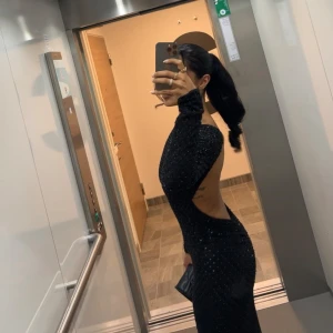 Embellished black dress - Supersnygg svart långklänning med glittriga detaljer och figurnära passform. Klänningen har långa ärmar och en djup öppen rygg som ger en riktigt elegant vibe. Perfekt för dig som vill sticka ut och glänsa på nästa stora kväll. Använd endast 1 gång . 34/36