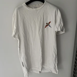Vit t-shirt med broderad fågel Axel Arigato - Snygg vit t-shirt från Axel Arigato med broderad fågel på bröstet och diskret logga på sidan. Klassisk passform och rund hals. Storlek XXS men passar XS