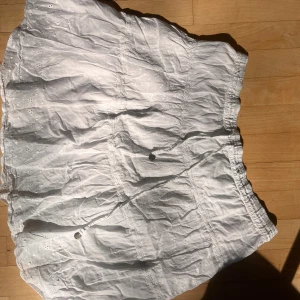 Vit broderad kortkjol med snörning - Supersöt vit kortkjol från HM. Kjolen har volanger, snörning i midjan och är gjord i tunn bomull🥰