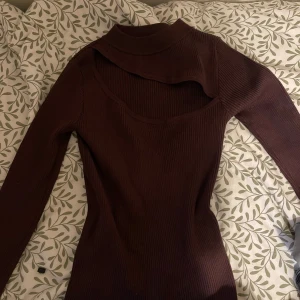 Mörkbrun ribbad polotröja med öppen frmasida - Snygg mörkbrun ribbad polotröja med lång ärm och unik öppen framsida-detalj. Tröjan har en tight passform och är perfekt för dig som vill sticka ut med en cool twist på klassisk stil.