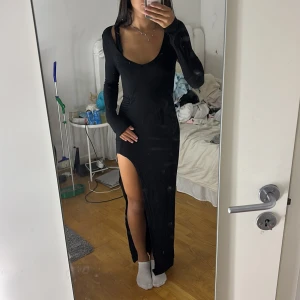 Svart långklänning med slits - Säljer en svart långklänning i storlek S med djup urringning och lång ärm. Klänningen har en hög slits på ena sidan som ger en snygg och edgy look. Figurnära passform som framhäver siluetten. Perfekt för dig som vill sticka ut.