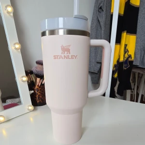 Ljusrosa Stanley axelväska - Säljer en ljusrosa axelväska från Stanley med stort handtag och lock med sugrör. Väskan har en stilren design och är perfekt för att bära med sig dryck. Märkets logga syns tydligt på framsidan. har använts några gånger men diskar sugröret innan den säljs💞