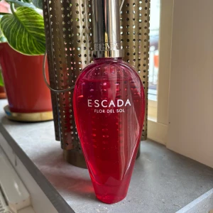 Escada Flor del Sol Eau de Toilette 100 ml - En färgstark parfym från Escada i en elegant rosa glasflaska med silverfärgad kork. Doften är Flor del Sol och flaskan rymmer 100 ml. Perfekt för dig som gillar fruktiga och blommiga dofter med en somrig känsla. Se bilder för återstående mängd. Säljs utan kartong!