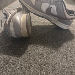 Nike Dunk i grått och vitt - Säljer ett par Nike Dunk sneakers i grått och vitt. Skorna har klassisk rund tå, platt sula och snörning framtill. Perfekta för dig som gillar stilrena och tidlösa sneakers med ikonisk Nike-design. Kontakta gärna vid frågor, pris:300kr vid snabb affär kan priset diskuteras 