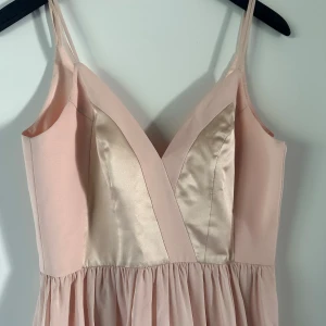 Ljusrosa långklänning från Zetterberg Couture - Supersöt ljusrosa långklänning från Zetterberg Couture för bal el bröllop med smala axelband och v-ringning. Klänningen har inslag av glansigt satinmaterial framtill och ett lätt, flygigt tyg i kjolen. Perfekt för speciella tillfällen. Använd en gång som brudtärna! Strl 38.