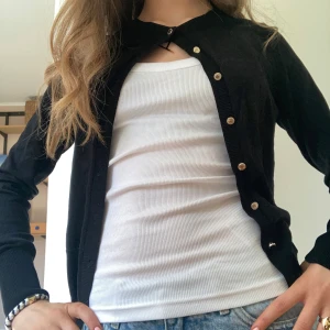 Svart kofta med guldknappar - Säljer en klassisk svart kofta med guldknappar. Koftan har lång ärm, rund halsringning och är i ett mjukt, tunt material. Perfekt att slänga över en topp eller t-shirt. Passar till mycket och är enkel att styla.