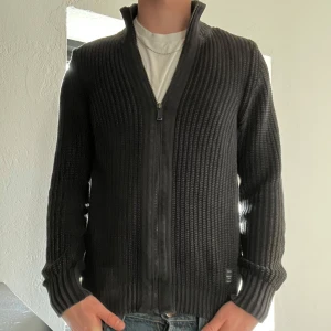 Replay cardigan  - Säljer en svart stickad cardigan jacka med dragkedja framtill. Jackan har ribbade muddar och en hög krage. Perfekt för lager-på-lager och passar till jeans eller andra byxor. Defekt vid armen. Skriv för fler bilder 