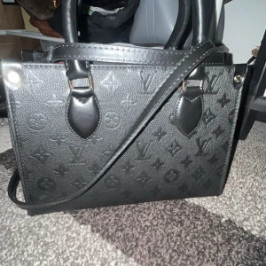 Svart axelväska  - Säljer en svart axelväska Väskan har både handtag och axelrem samt röd insida med guldfärgade detaljer och dragkedja. Perfekt för dig som vill ha en stilren och lyxig accessoar.