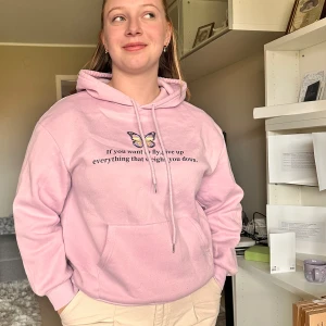 Ljusrosa hoodie med tryck och fjäril - Säljer en ljusrosa hoodie med tryck framtill och en liten fjäril ovanför texten. Tröjan har huva, magficka och långa ärmar. Perfekt för en avslappnad stil och supermjuk att ha på sig.