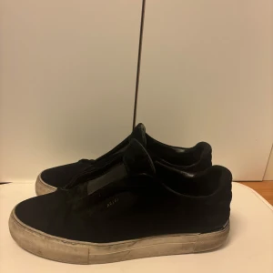 Axel Arigato skor - Säljer ett par svarta sneakers från Axel Arigato med platt vit sula och minimalistisk design. Skorna har rund tå och är tillverkade i mocka med diskret logga på sidan. Perfekta för en stilren vardagslook. Nypris på  2500kr. Finns ett litet jack på skon, men de märks inte. Mitt pris 399. Skriv för frågor eller annat!