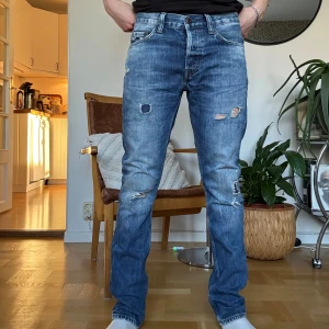 Blå slitna jeans från Crocker - Säljer ett par blå jeans från Crocker i modellen 306 Tapered. Jeansen har slitna detaljer och hål på benen.