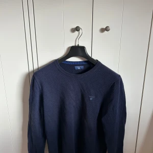 Gant tröja - Säljer en klassisk mörkblå stickad tröja från GANT med rund halsringning. Tröjan har diskret logga broderad på bröstet och är långärmad. Perfekt för lager-på-lager under kyligare dagar.