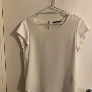 Vit topp från ONLY - Säljer en stilren vit topp från ONLY i storlek 34. Toppen har rund halsringning, korta ärmar och en diskret dragkedja i nacken. Perfekt för en enkel och fräsch look.