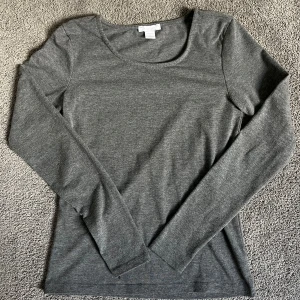Grå långärmad topp från Amisu - Säljer en enkel och stilren grå långärmad topp från Amisu. Tröjan har rund halsringning och är tillverkad i ett mjukt material som passar perfekt till vardags. Snygg att bära som den är eller under en kofta.