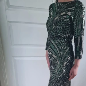 Grön paljettklänning med lång ärm - Säljer en glittrig grön långklänning med paljetter och lång ärm. Klänningen har ett geometriskt mönster och en elegant, figurnära passform. Perfekt för festliga tillfällen!Köpt i England..Om det behövs kan jag skicka bättre bilder på klänningen vid intresse 