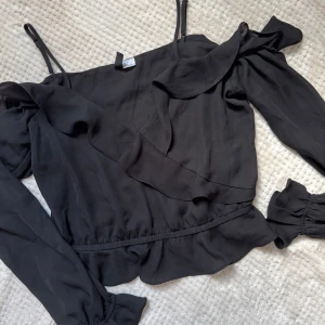 Svart topp - Svart omlottopp med volangdetaljer och långa ärmar. Toppen har smala axelband med offshoulder design 🖤Storlek M men är mer som en S