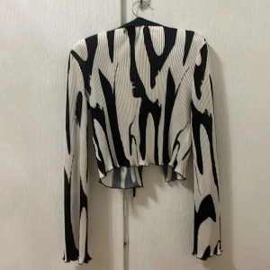 Svartvit mönstrad skjorta från SHEIN - Trendig skjorta från SHEIN i svartvitt abstrakt mönster. Skjortan har lång ärm, krage och knytning framtill. Materialet är lätt plisserat och ger en cool struktur. Perfekt för dig som vill sticka ut med din stil.