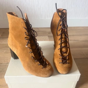Bruna mockaboots med snörning och klack - Säljer ett par snygga bruna boots i mocka från Sézane. Skorna har hög klack, snörning framtill och rund tå. Perfekta för att lyfta din outfit med en retrovibe. Dragkedja på insidan för enkel påtagning.