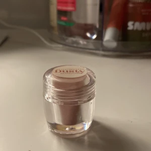 Makeup Mekka Dusty Shadow ögonskugga i färgen Joy - Säljer en Dusty Shadow ögonskugga från Makeup Mekka i färgen joy i en liten burk. Färgen är ljusrosa med skimrande finish, perfekt för att ge ögonlocken en mjuk och glittrig look. Kommer i en transparent plastförpackning med skruvlock. Aldrig använd. 