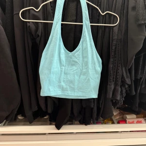 Ljusblå croppad linnetopp - Säljer en ljusblå croppad linnetopp med djup urringning och brottarrygg. Perfekt för varma dagar eller som ett lager under en skjorta. Enkel och stilren design.