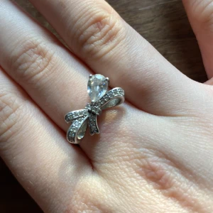 SHE’S ICED RING - Säljer en silverring med en stor, droppformad klar sten och en rosettdetalj framtill. Ringen är i äkta silver (stämplad 925) och har små gnistrande stenar på rosetten för extra bling. Originellt så kostar den 560kr men jag har ingen användning utav den längre pga olika anledningar. Inget är fel på ringen! Pris kan diskuteras såklart ❤️