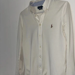 Vit skjorta från Ralph Lauren - Klassisk vit skjorta från Ralph Lauren med broderad logga på bröstet. Skjortan har knappar hela vägen och button-down krage. Perfekt till många olika outfits och enkel att styla. Använt ett par gånger typ 3 gånger, Utan fläckar eller något annat. Köpt den för 800 kronor, säljer pga att den blev mindre. Priset kan diskuteras, passar för S st, blev liten pga tvätt. Priset kan diskuteras!!