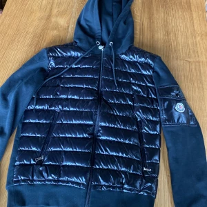 Svart moncler cardigan med huva - Säljer en fet, svart cardigan från Moncler med glansig framsida och huva. Jackan har dragkedja, två fickor fram. Perfekt för kalla dagar🥶.
