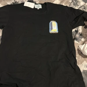 Svart t-shirt från Casablanca med tryck - Svart t-shirt från Casablanca med färgglatt grafiskt tryck och texten 'Casa Blanca' på bröstet och ryggen.  Fick den i present men den var för liten, Storlek L på tröjan men passar storlek M ochså 