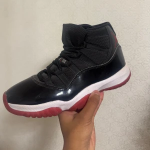 Nike Air Jordan 11 Retro 'Bred' - Säljer ett par klassiska Nike Air Jordan 11 Retro 'Bred' med svart mesh och lackdetaljer, vit mellansula och röd yttersula. Ikonisk Jumpman-logga på hälen och snörning framtill. Perfekta för dig som gillar streetwear och sneakerskultur. Boxen till skorna kommer med. Kan erbjuda tvättning. Går att förhandla priset!