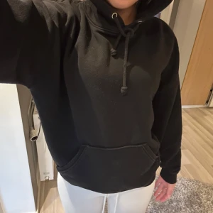 Svart hoodie med ficka - Säljer en svart hoodie med huva och band. Tröjan har en stor magficka och är i en oversized passform. Perfekt för dig som gillar en avslappnad stil.
