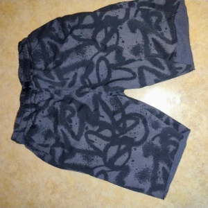 Svarta shorts med grått mönster från H&M - Säljer ett par svarta shorts från H&M med grått abstrakt mönster. De har resår i midjan och är tillverkade i ett mjukt material som passar perfekt för avslappnade dagar.