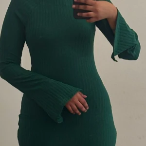 Mörkgrön ribbad långärmad maxi klänning - Säljer en snygg grön ribbad klänning med lång ärm och utsvängda ärmslut. Klänningen har en tight passform och är perfekt för dig som gillar stilrena plagg med det lilla extra. Jag har endast haft klänningen en gång, känner att den inte kommer till någon användning längre.